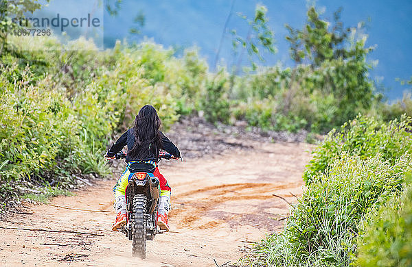 Frau fährt mit ihrem Geländemotorrad auf einem Waldweg in Pak Chong / Thailand