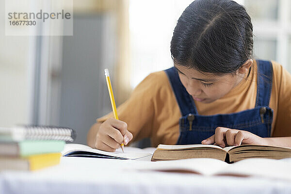 Asiatisches Mädchen  das zu Hause liest und Hausaufgaben macht