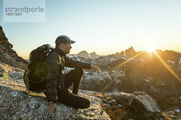 Rucksacktourist sitzt auf einem Berggipfel und genießt den Blick auf den Sonnenuntergang.
