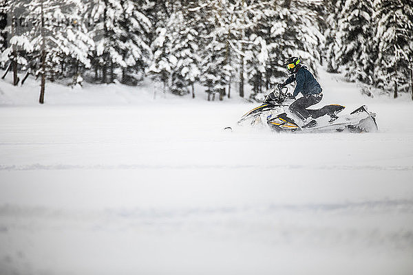 aktiver Mann  der während eines Wochenendausflugs mit dem Motorschlitten durch den Tiefschnee fährt.