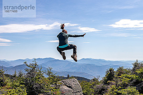 Junge Frau  die auf dem Gipfel eines Berges einen Karatekick macht.