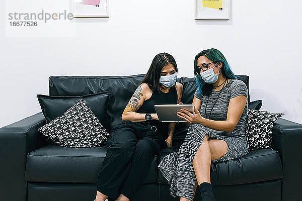 Zwei Geschäftsfrauen mit Masken benutzen in der Büropause ein Tablet