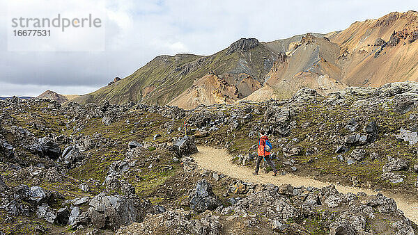 Junger Mann beim Wandern auf dem felsigen Pfad in Landmannalaugar