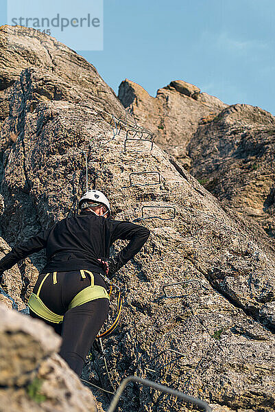 Konzept: Abenteuer. Bergsteigerin mit Helm und Klettergurt. Rückwärts. Ausruhen vor dem Weitersteigen. Via ferrata in den Bergen.