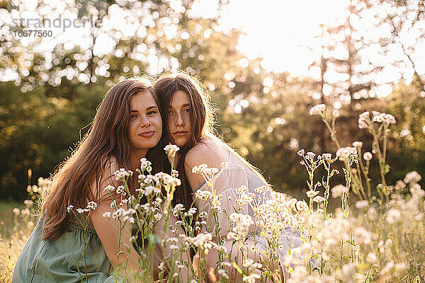 Porträt eines lesbischen Paares  das inmitten von Blumen im Sommerwald sitzt