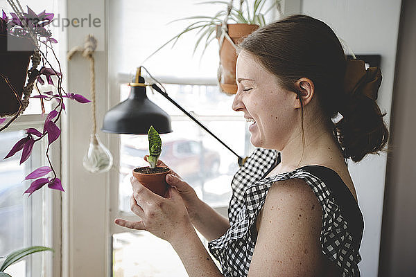 Junge Frau lächelt und lacht über eine ihrer Pflanzen in einem hellen Raum