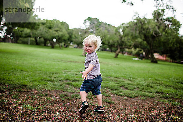 Zweijähriges Kind blickt beim Laufen durch den Park auf die Kamera zurück