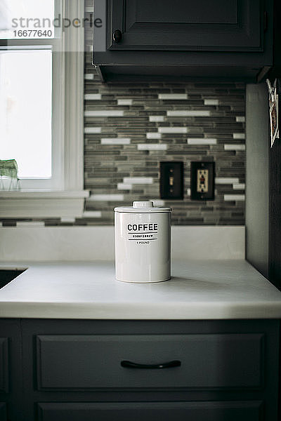 Ein weißes Glas mit gemahlenem Kaffee steht auf einer weißen Arbeitsplatte in einer Küche.