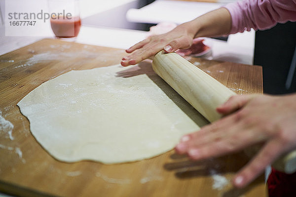 Detail der Hände zu Hause beim Herstellen und Ausrollen des Pizzateigs