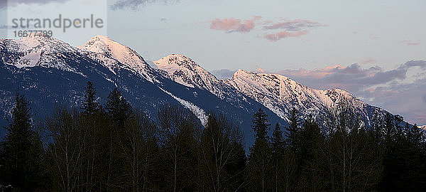 An einem Frühlingstag in den Coast Mountains von British Columbia geht die Sonne über den schneebedeckten Bergen unter.