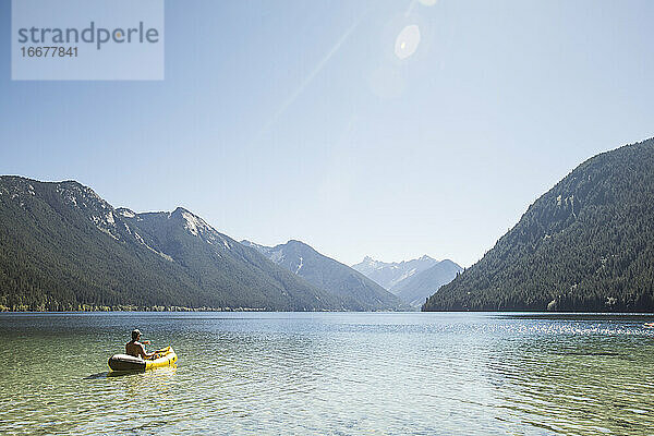 Rückansicht eines Mannes  der auf dem Chilliwack Lake mit einem Schlauchboot paddelt.