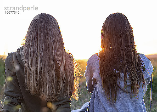 zwei Mädchen  die Rücken an Rücken den Sonnenuntergang beobachten