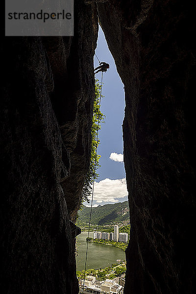 Blick auf die Silhouette eines Bergsteigers  der sich an einem Bergspalt abseilt