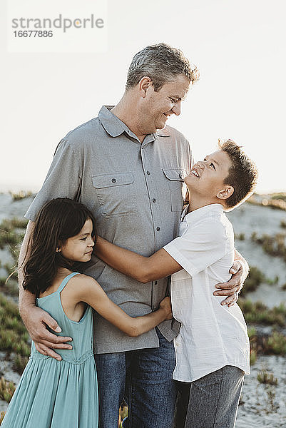 Vater  Mitte 40  in grauem Hemd  umarmt seinen Sohn und seine kleine Tochter