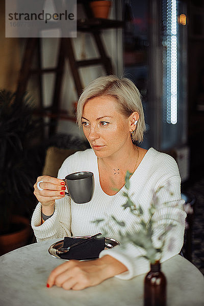 Blonde osteuropäische Frau trinkt Kaffee und sitzt am Tisch