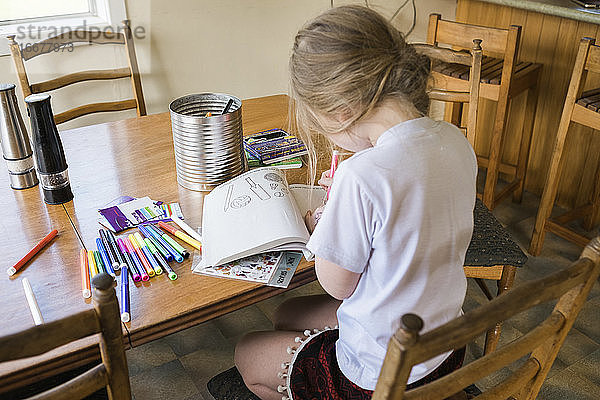 Junges Mädchen sitzt an einem Tisch und malt und zeichnet