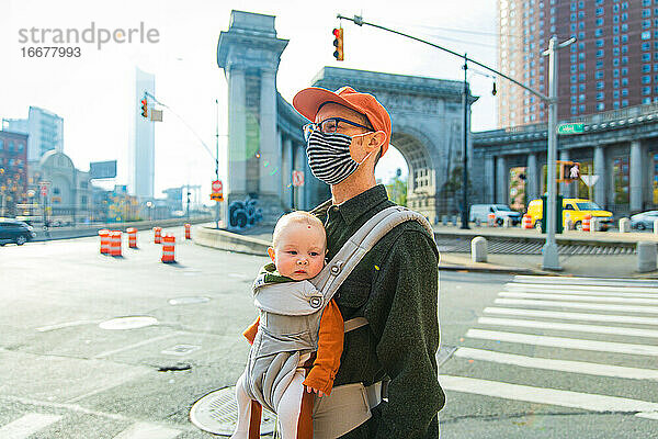 Vater trägt seine Tochter in einer Babytrage  während er während der Coronavirus-Pandemie auf der Straße geht