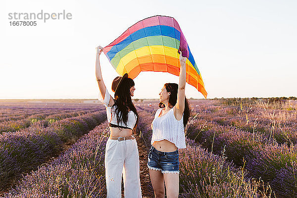 Freundinnen schauen sich in einem Lavendelfeld an und schwenken eine Igbt-Flagge