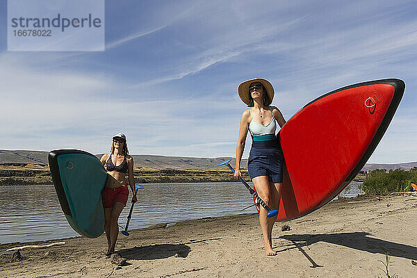 Zwei Frauen tragen ihre SUPs aus dem Columbia River in Oregon.