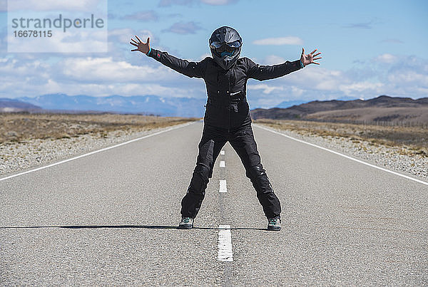 Frau in Motorradkleidung steht in der Mitte einer leeren Autobahn