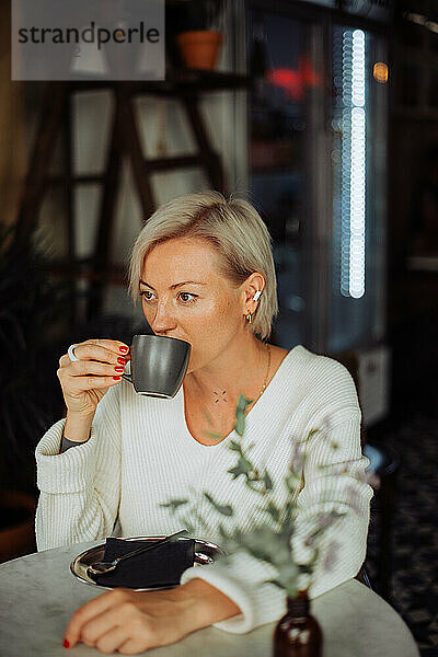 Stilvolle blonde Frau trinkt Kaffee und sitzt am Tisch im Café