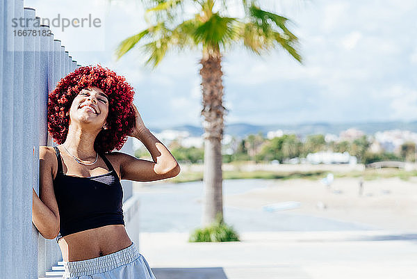 Frau mit rotem Afro-Haar stehend mit Strand im Hintergrund.