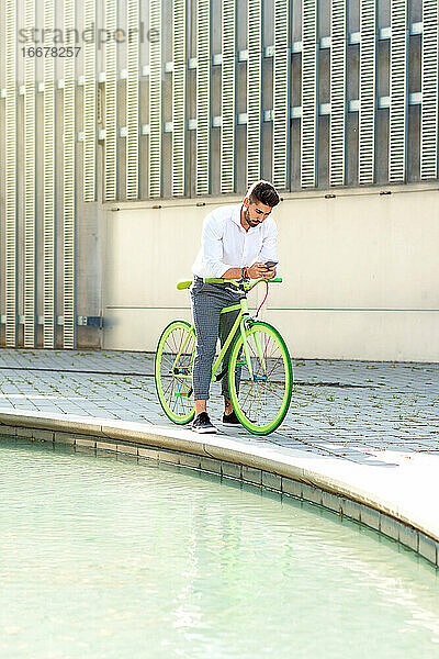 Outdoor-Porträt eines gut aussehenden jungen Mannes mit Mobiltelefon und Fahrrad mit festem Gang auf der Straße.