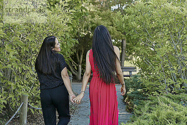 Junge Frauen Paar hält die Hände zu Fuß auf grünem Gras in einem Park an einem sonnigen Tag. romantisches Konzept