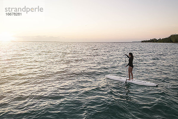 Frau Paddleboarding auf dem Meer gegen den Himmel bei Sonnenuntergang