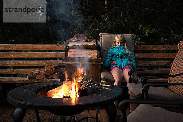 Tween Girl Sitting ruhig in der Nähe von Outdoor-Feuerstelle in der Abenddämmerung