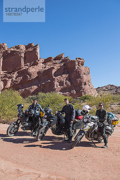 Gruppe von Freunden steht neben Reisemotorrädern in der Wüste