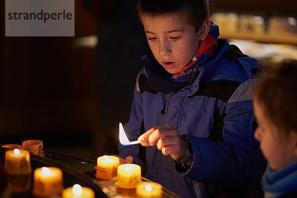 ein Kind zündet mit einem Streichholz eine Kerze in einer Kirche an