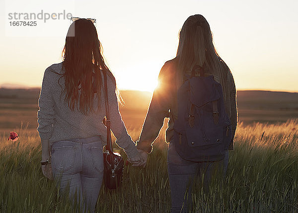 zwei Frauen halten sich bei Sonnenuntergang auf einem Feld an den Händen