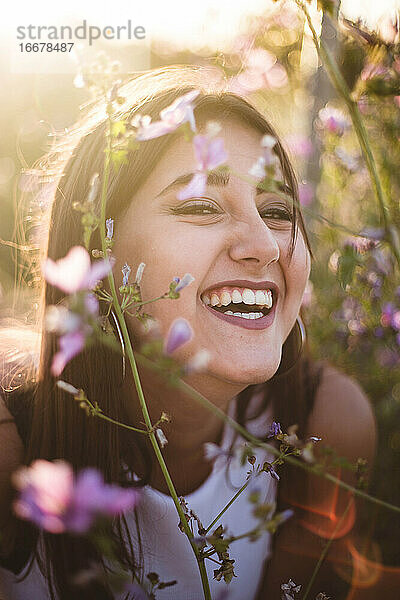 Teenager schaut in die Kamera und lacht zwischen Blumen in der Natur
