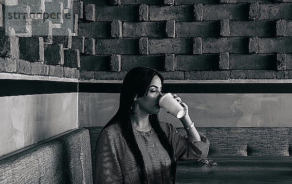 Frau genießt einen Kaffee  Backsteinmauer im Hintergrund
