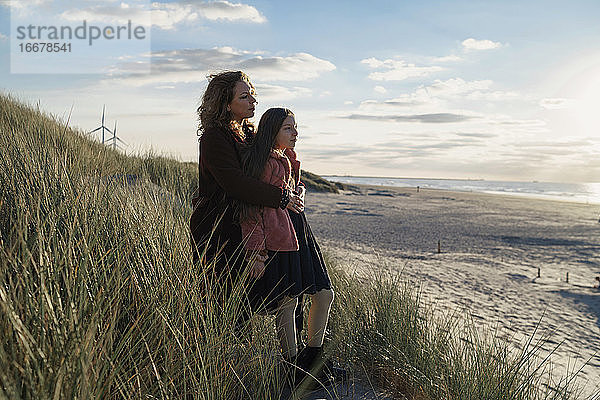 Mutter und Tochter am Strand stehend mit Blick aufs Meer