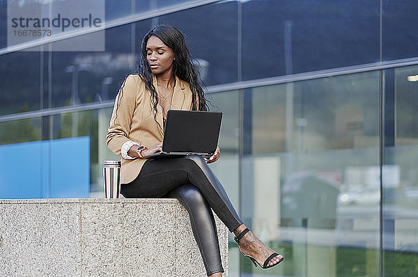 Porträt einer schwarzen Geschäftsfrau im braunen Anzug  die telefoniert und einen Laptop in der Hand hält