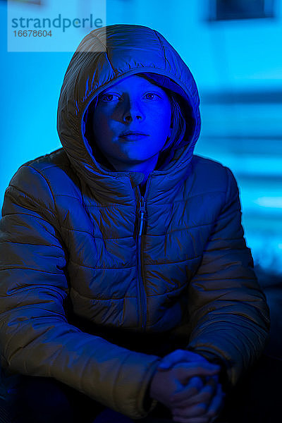 Porträt eines jungen Menschen  der in einem nur mit blauem Licht beleuchteten Raum sitzt
