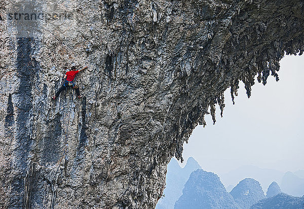 Mann klettert auf den natürlichen Felsbogen auf dem Mondberg in Yangshuo