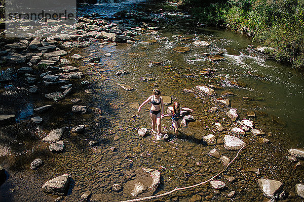 Draufsicht auf zwei Schwestern  die durch einen seichten Bach laufen