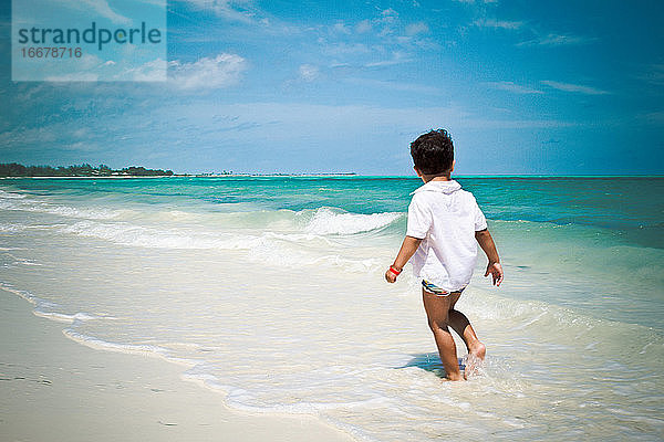 Kleiner Junge spaziert am Strand und beobachtet das karibische Meer