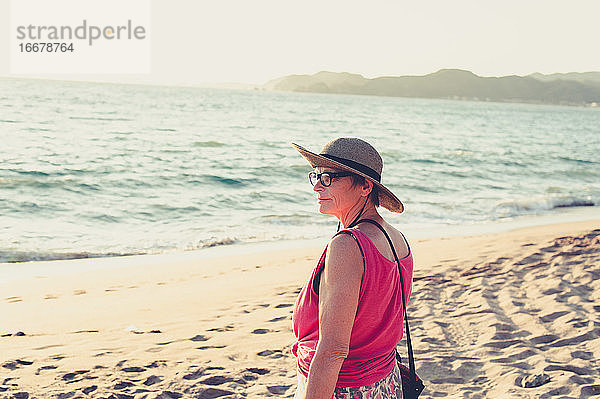 Ältere Frau lächelt und blickt auf das Meer am Strand