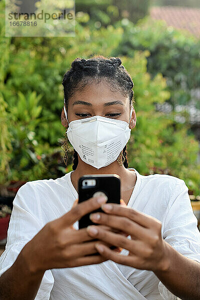 Junge schwarze Frau mit Gesichtsmaske  die ein Smartphone benutzt