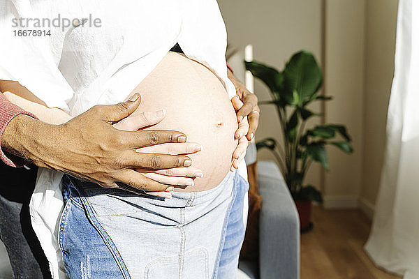 Nahaufnahme eines Mannes  der den Bauch seiner schwangeren Frau umarmt. Konzept der Elternschaft