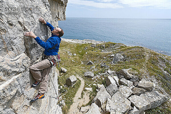 Mann klettert auf Kalksteinfelsen in der Nähe der Küste von Swanage / UK