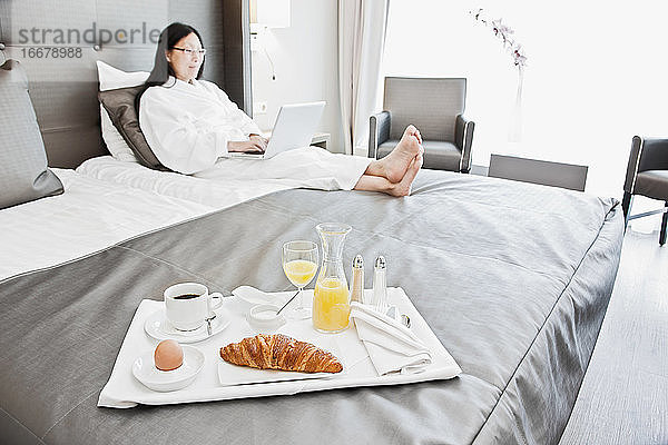 Geschäftsfrau beim Frühstück im Bett in einem luxuriösen Business-Hotel