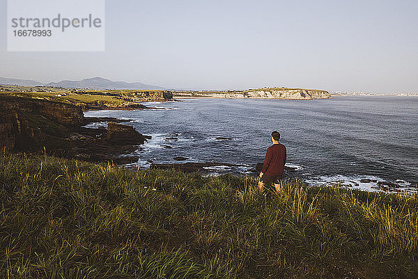 Ein junger Mann steht vor einer Klippe  die an der Küste beginnt  Kantabrien  Spanien
