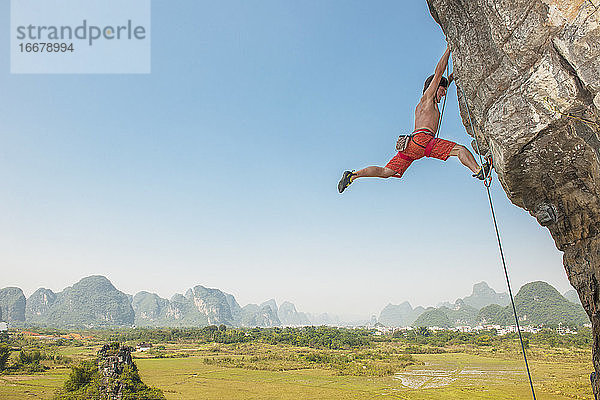 Männlicher Kletterer zieht sich an einem überhängenden Felsen in Yangshuo / China hoch