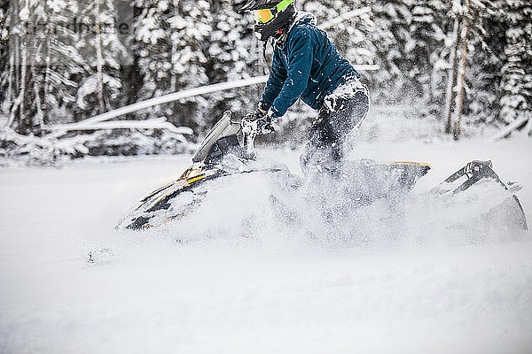Seitenansicht eines Mannes  der mit dem Motorschlitten durch tiefen Schnee fährt.