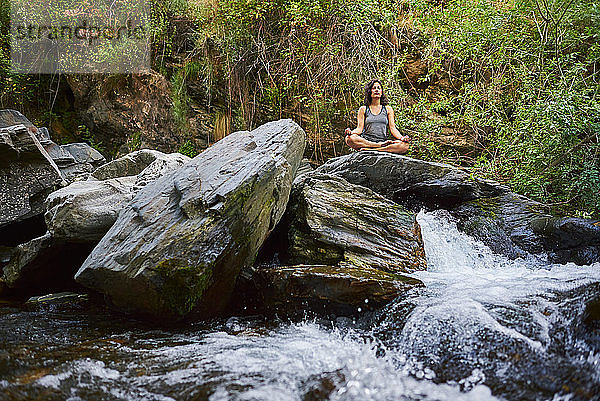 Junge Frau übt Yoga in einem Fluss. Sie ist mitten in der Natur.